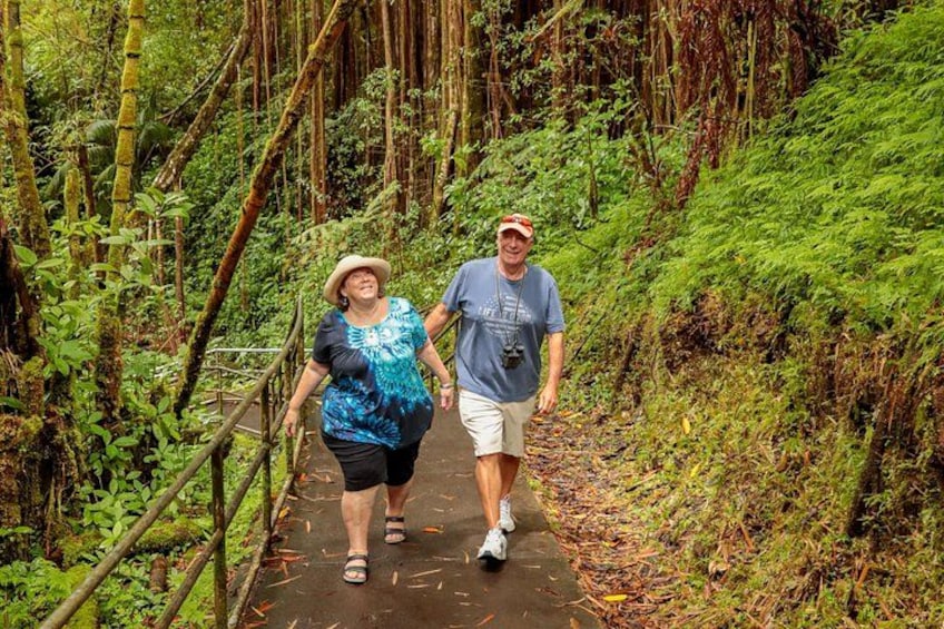 Two people walking on a path surrounded by dense green foliage and bamboo. 5