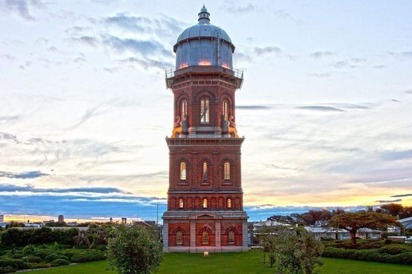 A tall brick tower with a dome, surrounded by greenery and a sunset sky. 4