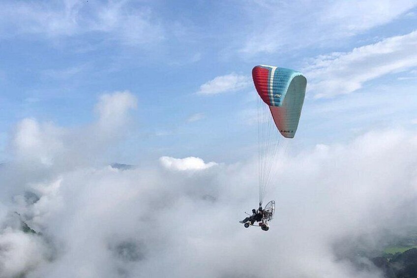 A paraglider flying above clouds with a colorful parachute. 1