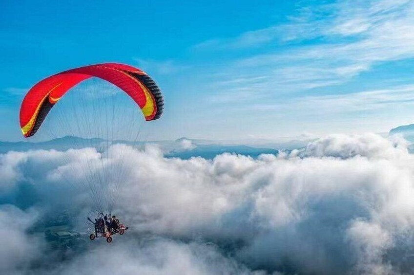 A paraglider above clouds with a red and yellow parachute. 4