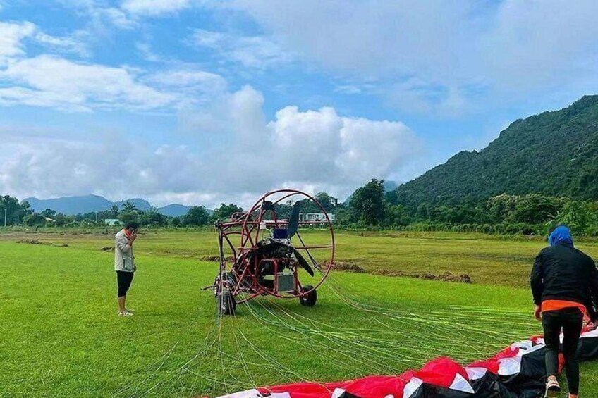 A person operating a red agricultural machine in a field with mountains in the background. 3