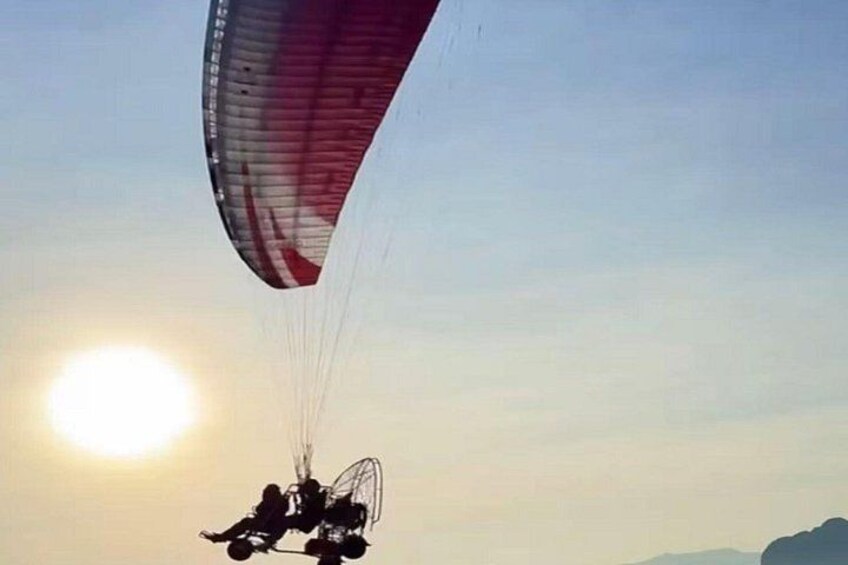 A paraglider with a red and white parachute flying near the sun. 2