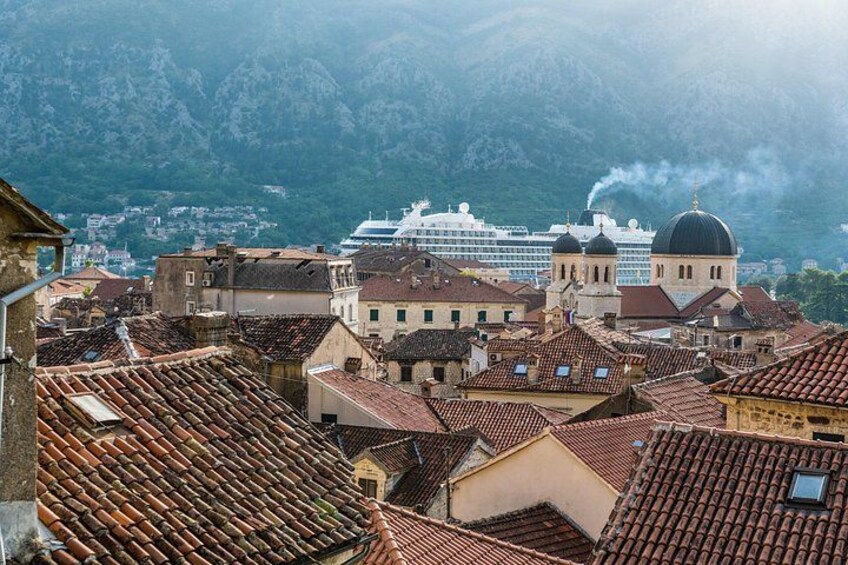 A coastal cityscape with terracotta-roofed buildings, a cruise ship, and a mountain backdrop. 2