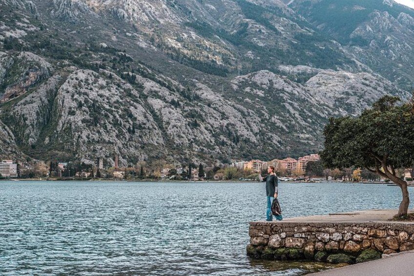 Une personne se tient près d’un mur de pierre, surplombant un lac avec des montagnes en arrière-plan. 2