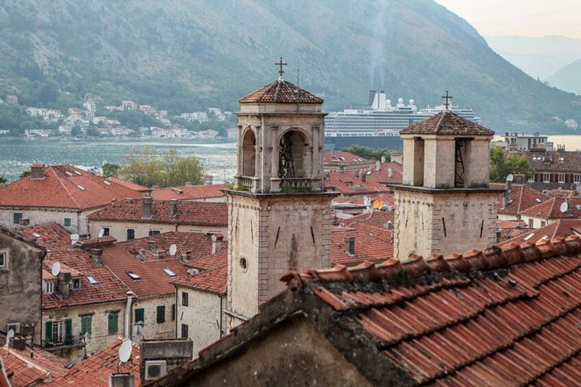 Une ville côtière aux bâtiments aux toits rouges, avec deux tours imposantes et un navire de croisière en arrière-plan. 3