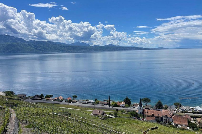 Un lago con un pueblo en primer plano, viñedos y montañas al fondo. 4