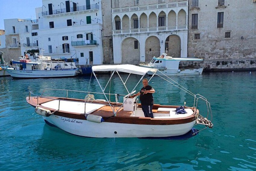 A small boat named 'La giostra del mare' docked in a harbor with buildings in the background. 1