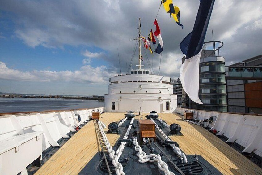 Cubierta de barco con superestructura blanca, varias banderas y cubierta de madera. 2