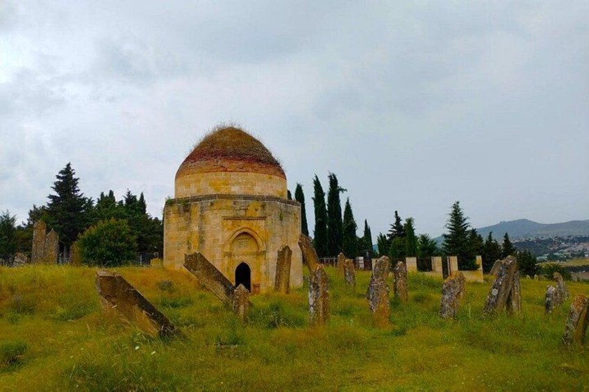 A historic stone building with a dome, surrounded by gravestones in a grassy field. 2