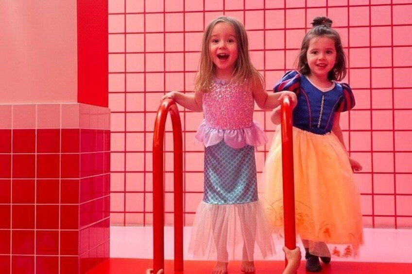 Dos niños vestidos con colores brillantes de pie en un área con baldosas y barandas rojas. 5