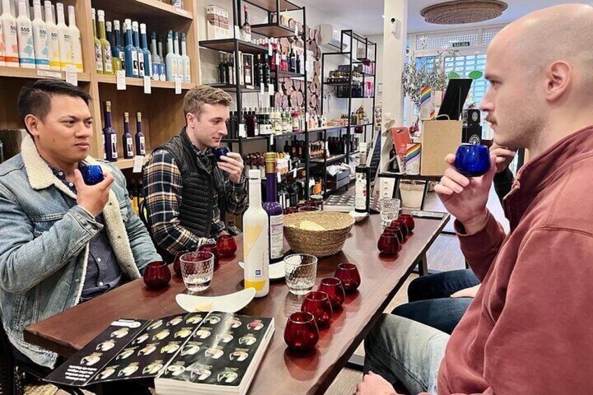 Three people sitting at a table in a store with various bottles and glasses. 1