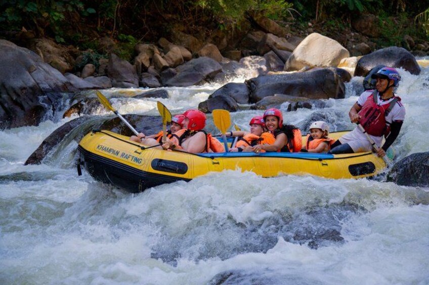 A group of people rafting on a yellow raft with a river and rocks in the background. 3