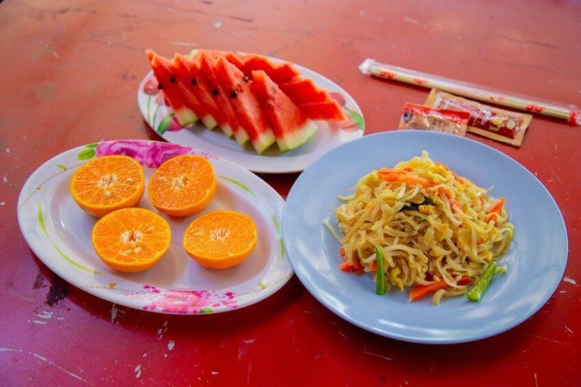 Three plates of food on a red table: one with watermelon, one with orange slices, and one with noodles. 2