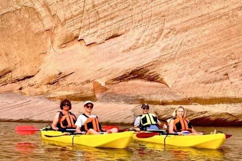 Three people kayaking in yellow kayaks on a calm river with a rocky canyon in the background. 2