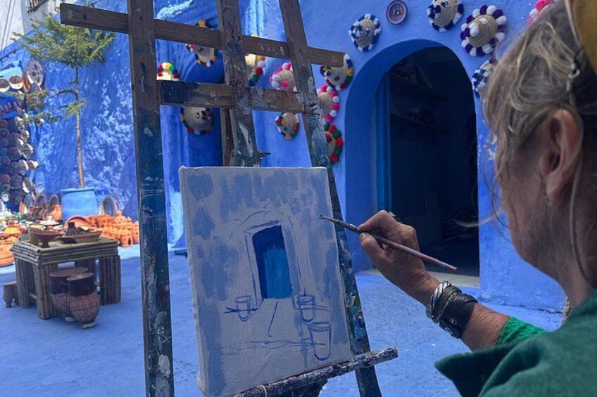 A person painting on an easel with a blue door sketch, surrounded by colorful decorations and a blue archway. 3