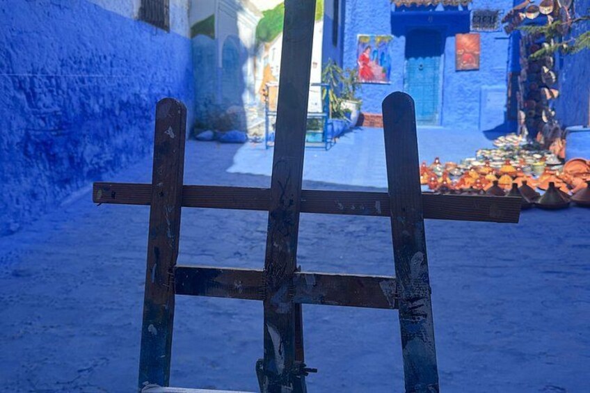 A wooden easel in a blue-painted alleyway with a street scene in the background. 4