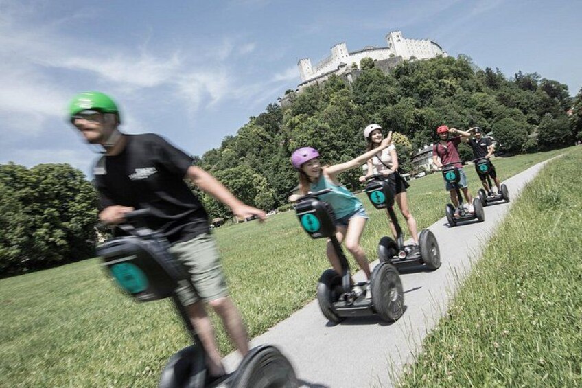 Des personnes se déplacent à bord de Segways sur un chemin aménagé dans un parc, avec un château en arrière-plan. 1