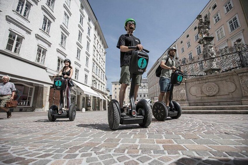 Des personnes se déplacent en Segway sur une rue pavée, avec des bâtiments historiques et une fontaine en arrière-plan. 4