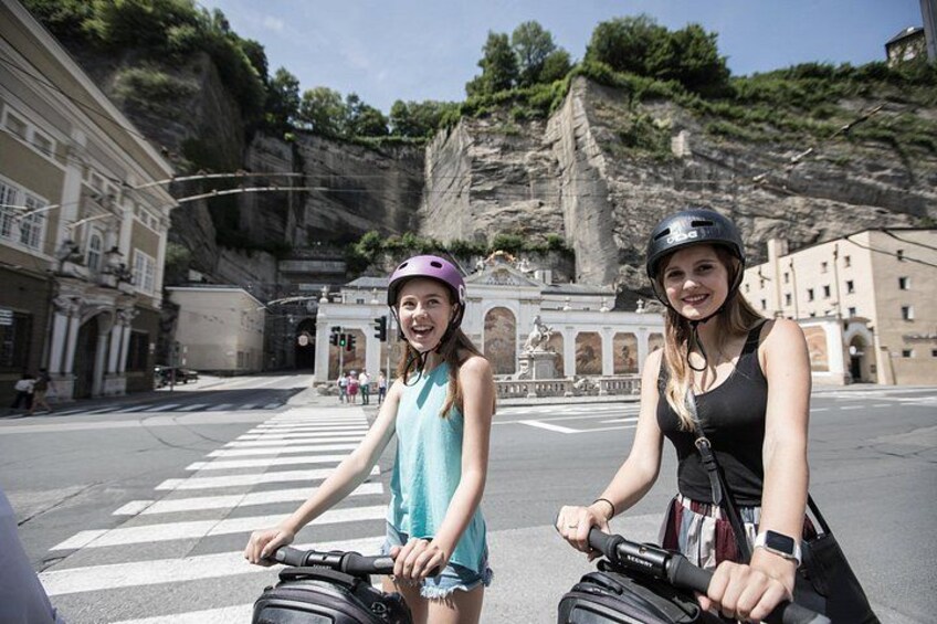 Deux personnes à vélo, portant des sacs à dos, traversent un passage piéton, et on aperçoit une falaise rocheuse en arrière-plan. 2