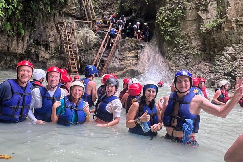 A group of people in water with helmets and life vests, a rocky waterfall, and a wooden ladder. 1