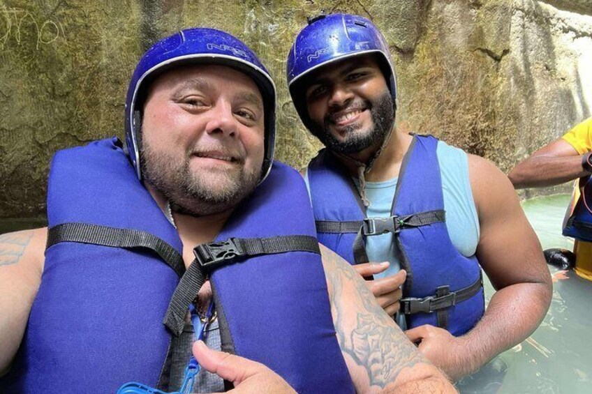 Zwei Personen mit blauen Helmen und Schwimmwesten stehen in der Nähe eines Gewässers. 1