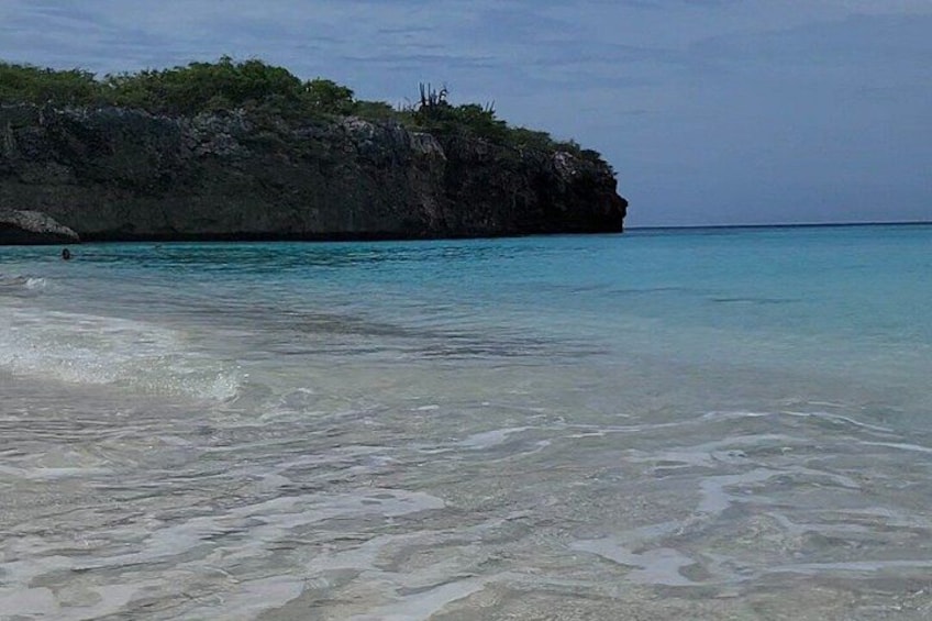 Ein Strand mit klarem türkisblauem Wasser, einem felsigen Felsen und spärlicher Vegetation. 2