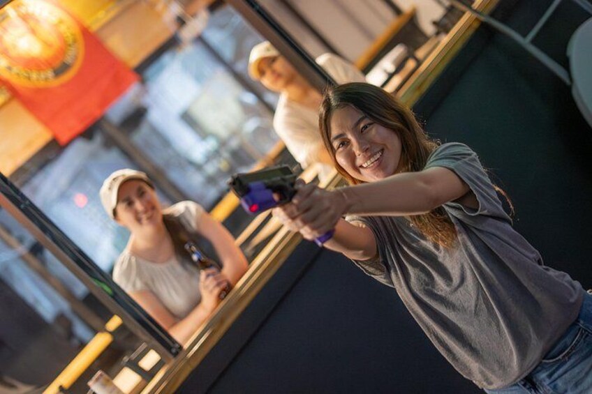 A person holding a camera, another person in the background holding a drink, and a reflection in a mirror. 4
