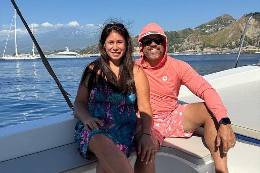 A couple on a boat with a mountainous landscape and sailboats in the background. 2