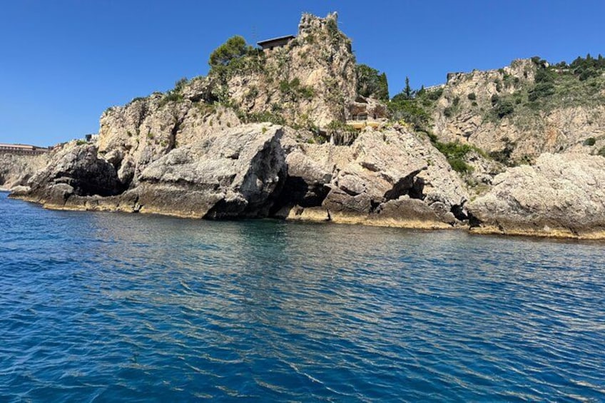 A rocky coastline with a building on top, clear blue water, and a clear sky. 2