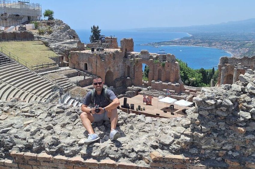 A man sitting on ancient ruins with a view of the sea and a city in the background. 5