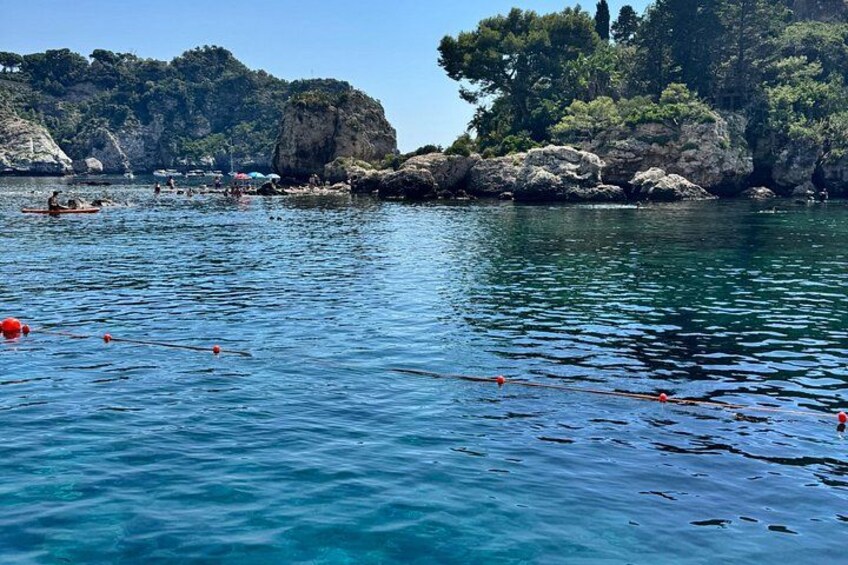 A calm body of water with boats, rocky cliffs, and trees. 5