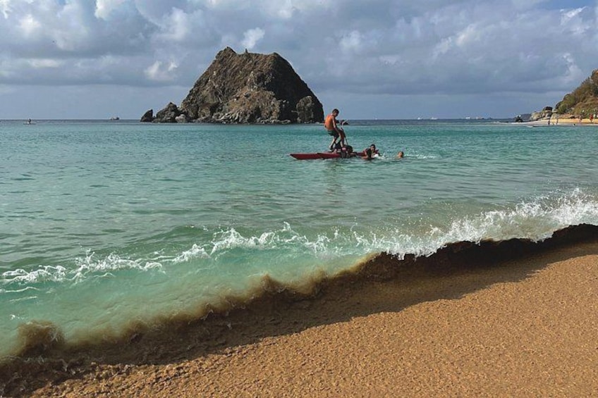Una spiaggia con acque cristalline turchesi, un promontorio roccioso e una persona su un paddleboard rosso. 1
