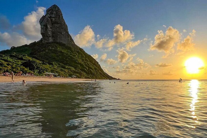 Una spiaggia con una roccia imponente, acqua calma e un tramonto. 3