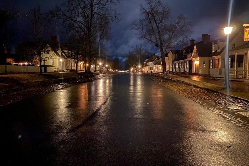 Eine nasse Straße bei Nacht, mit Häusern auf einer Seite und einer Straßenlaterne auf der anderen. 5