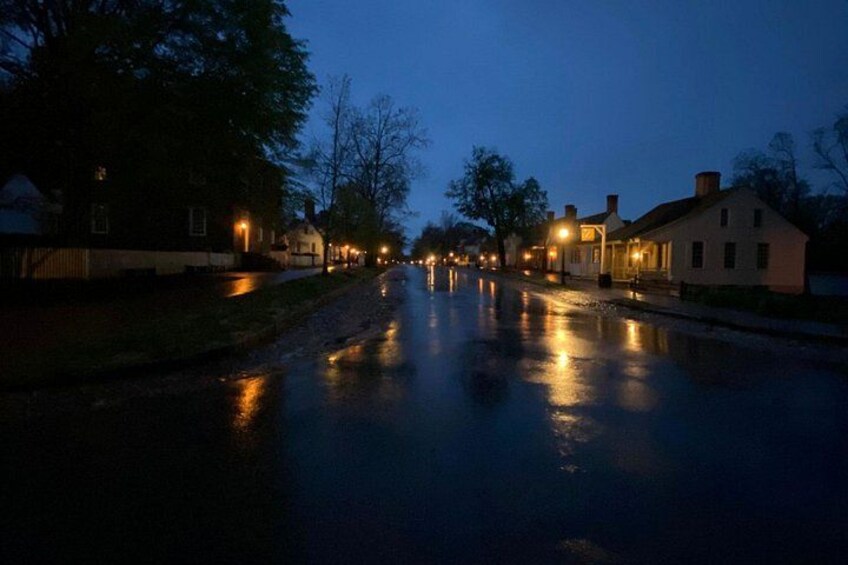 Eine feuchte Straße im Dämmerlicht mit Häusern an beiden Seiten und Straßenlaternen, die die Umgebung erhellen. 4