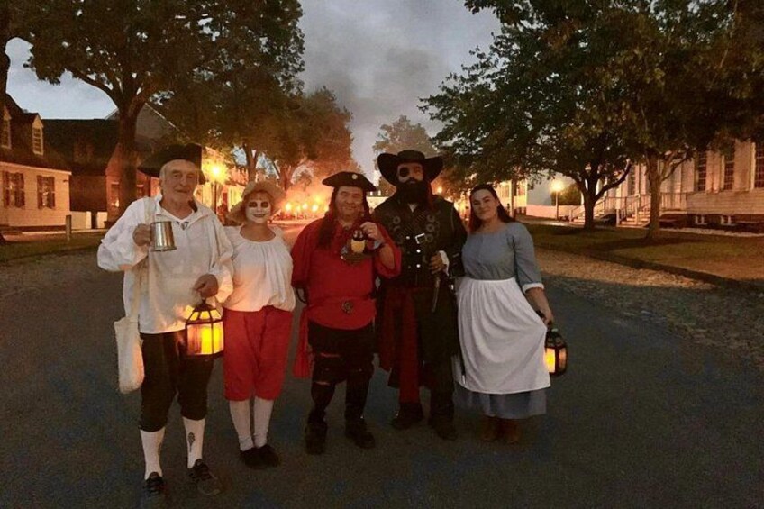 A group of people in historical costumes standing on a street with trees and buildings in the background. 2