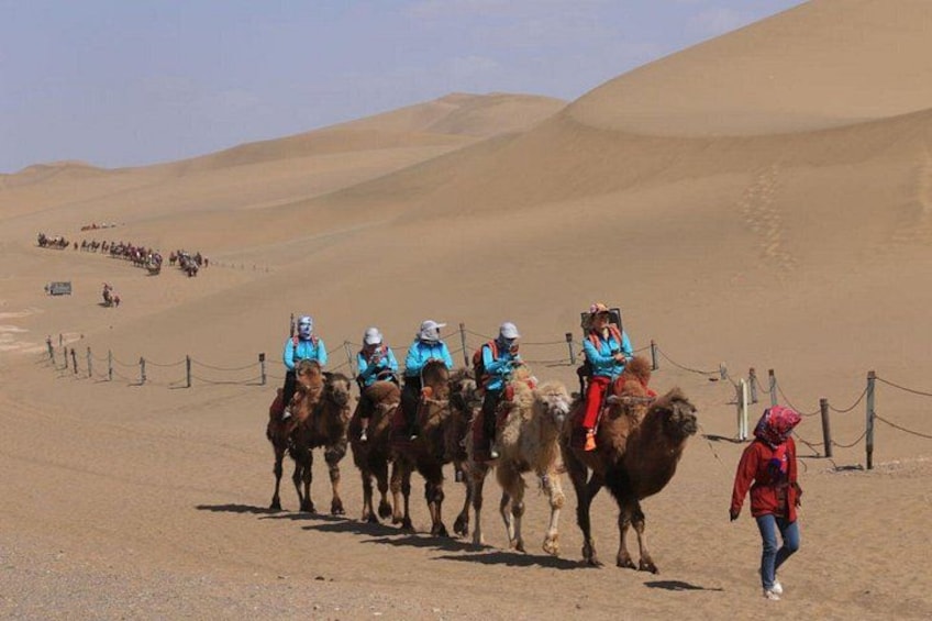 En gruppe mennesker rider på kameler i et ørkenlandskab med sandklitter. 3
