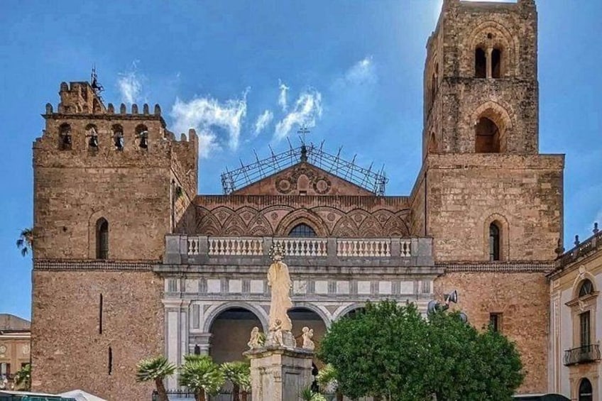 A historic building with two towers, a central arched entrance, and a statue in front. 1