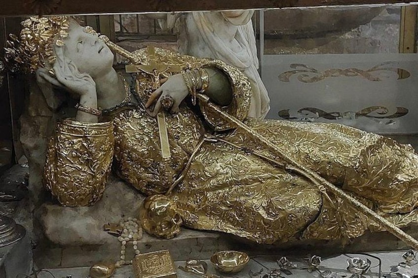 A statue of a reclining figure adorned with intricate golden patterns, surrounded by smaller golden objects. 5