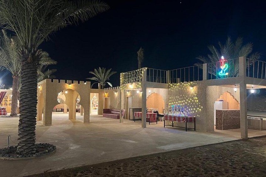 Een goed verlicht buitengebied met palmbomen, een overdekte zithoek en decoratieve verlichting. 3