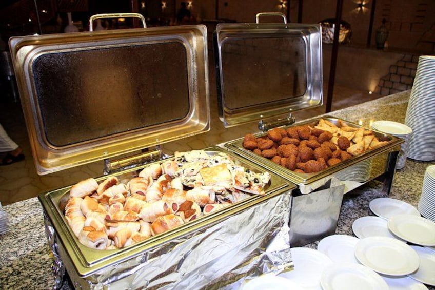 Een buffet met diverse gerechten, waaronder gebak en gefrituurd voedsel, met opschepbestek en borden. 4