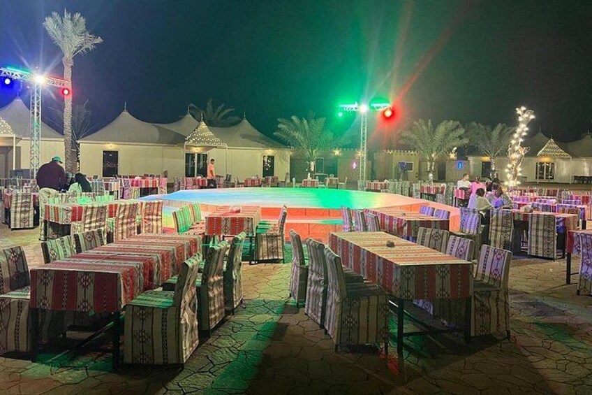 Een terras buiten met tafels en stoelen, een zwembad en tenten op de achtergrond. 2