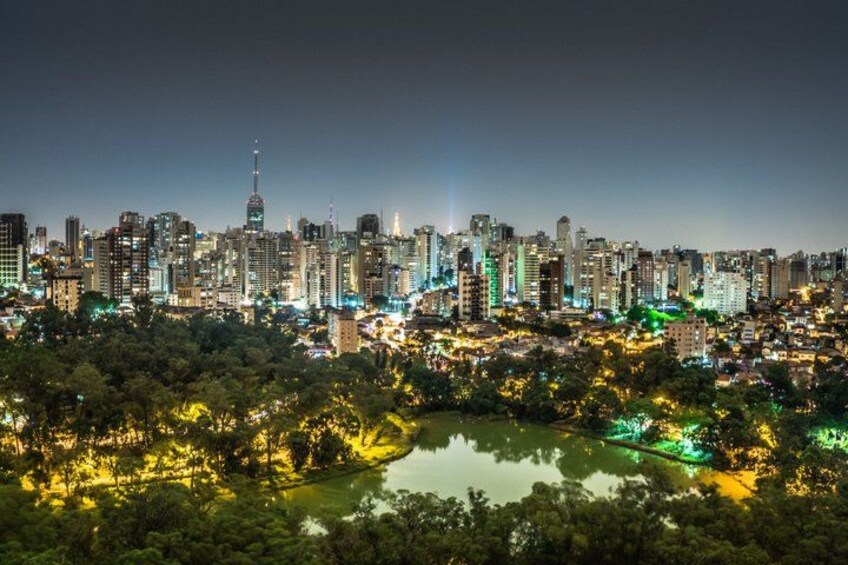 A city skyline at night with illuminated buildings and a body of water in the foreground. 2