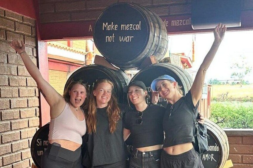 A group of people posing with large beer barrels, one barrel has text that reads 'Make mezcal not war.' 4