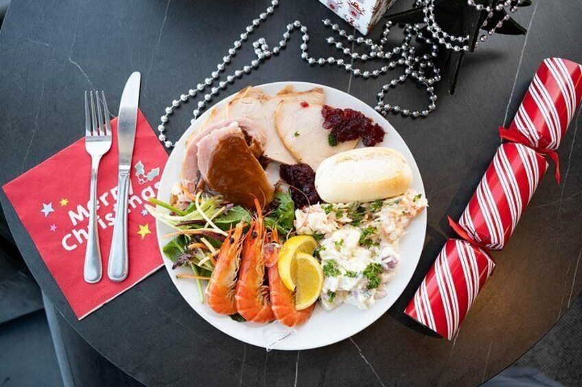 Un plato de comida con diversos ingredientes como camarones, pan y una ensalada, sobre una mesa con un mantelito rojo y un adorno navideño. 2
