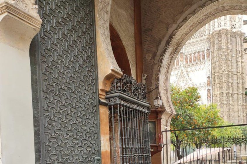 Een sierlijk ijzeren hekwerk met ingewikkelde patronen, een stenen muur met een geometrisch ontwerp, en een glimp van een historisch gebouw op de achtergrond. 3