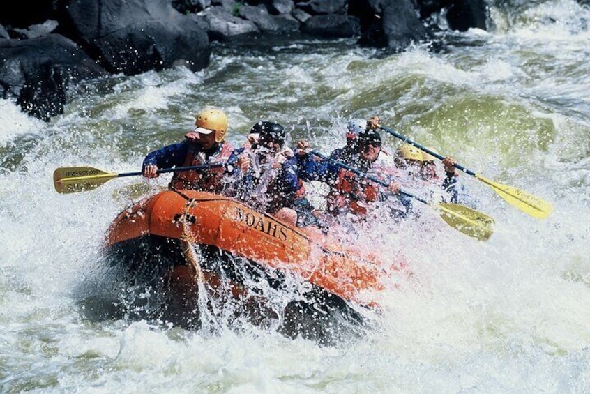 Un groupe de personnes à bord d’un radeau orange naviguant dans des rapides aux eaux tumultueuses. 2