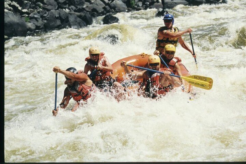 Un groupe de personnes à bord d’un radeau pneumatique naviguant sur une rivière à courant rapide. 3