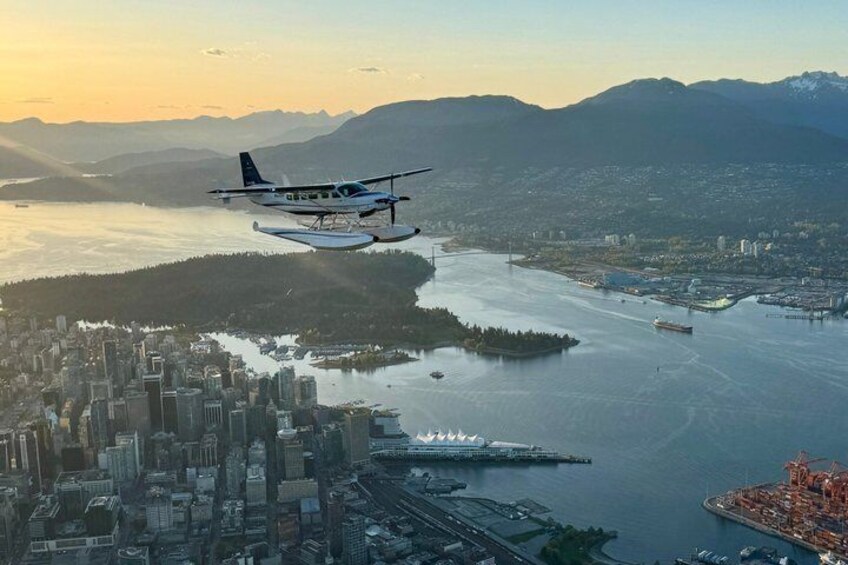 A seaplane flying over a city with a large body of water, mountains in the background, and a bridge. 4