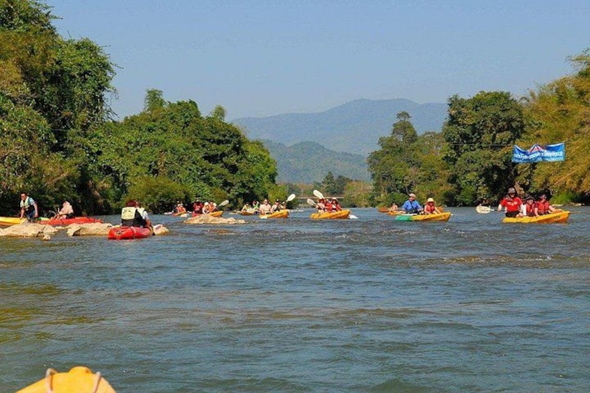 A group of people kayaking on a river surrounded by lush greenery and hills. 2